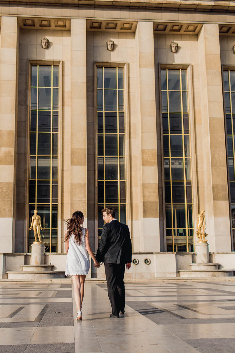 Bride and groom walk in the plaza between gold statues, Palais de Chaillot, Paris, France