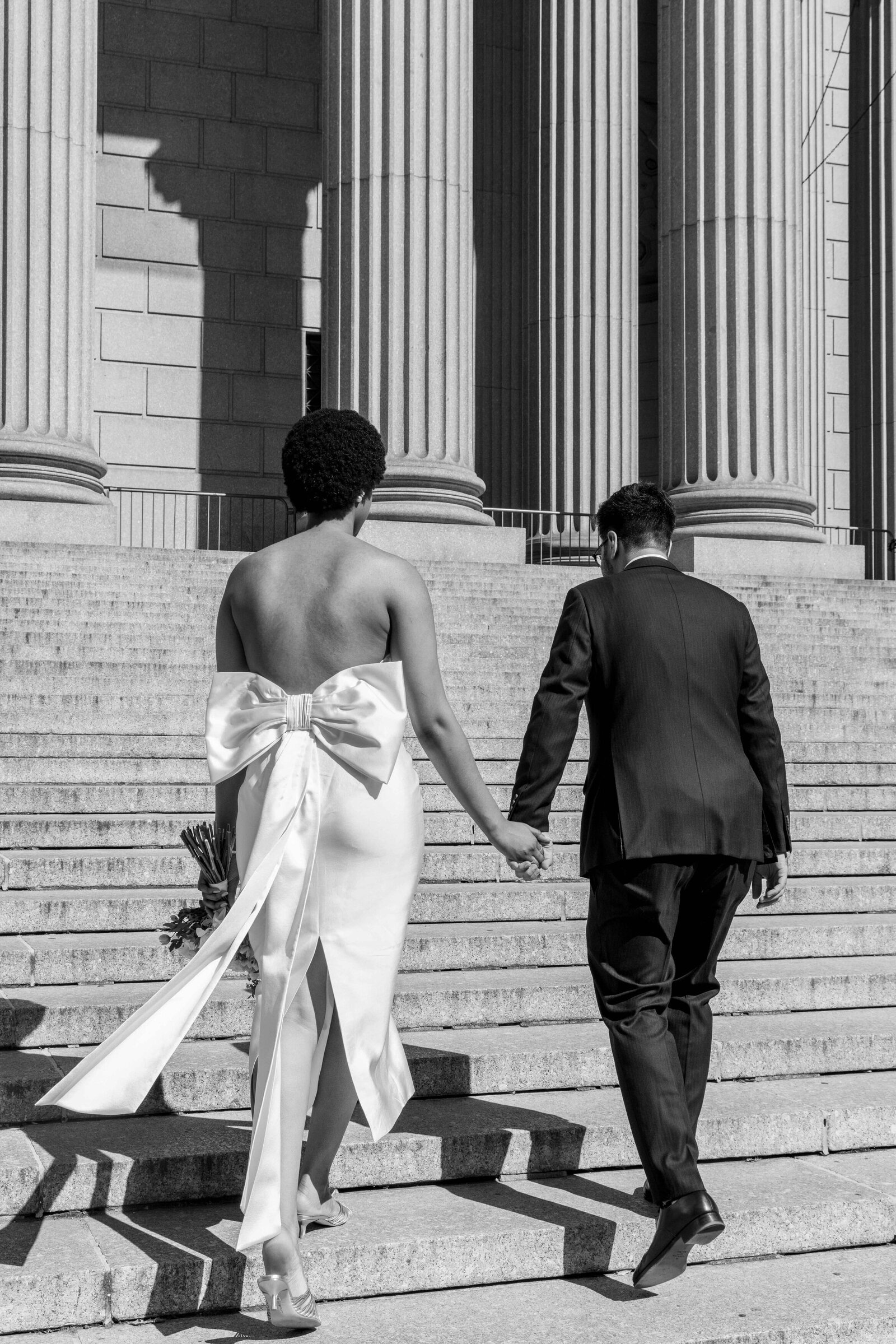 Black and white photo of a couple holding hands and walking up a staircase.