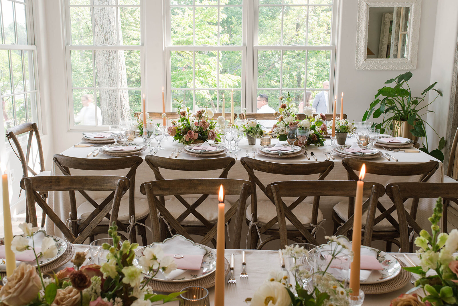 Inside a micro-wedding reception with long tables with brown wooden chairs and neutral, garden-style tables decor including wispy florals and taper candles.