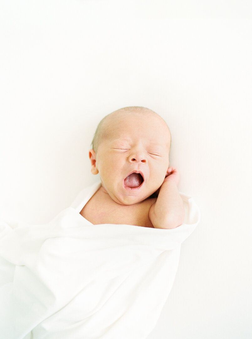 Newborn in white swaddle is yawning