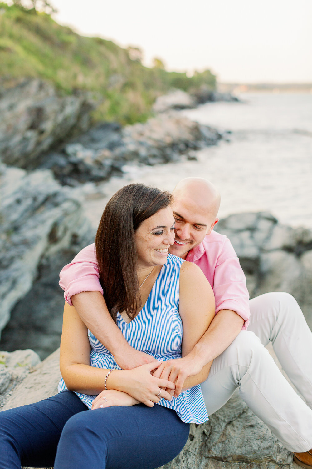 Couple sitting on rocks by the water with their arms around each other.