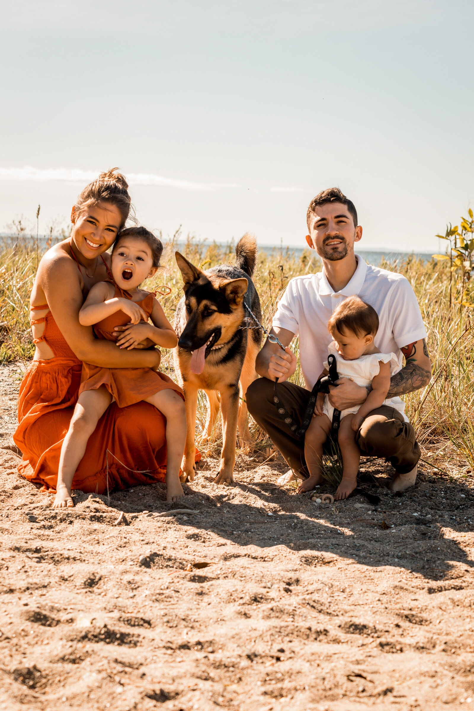 family smiling with their dog on the beach