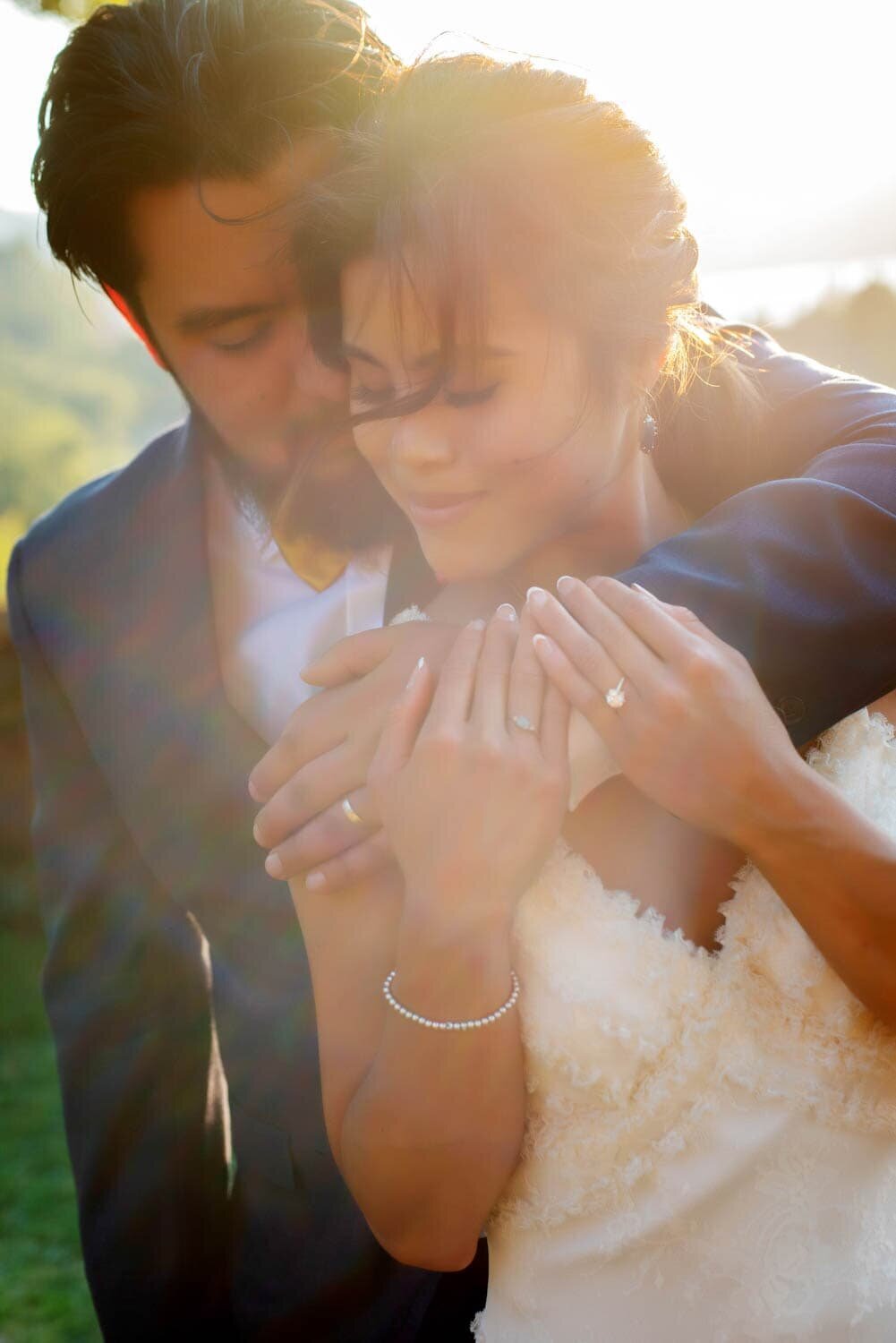 a groom hugs a bride bathed in sunlight with her hair blowing in the wind