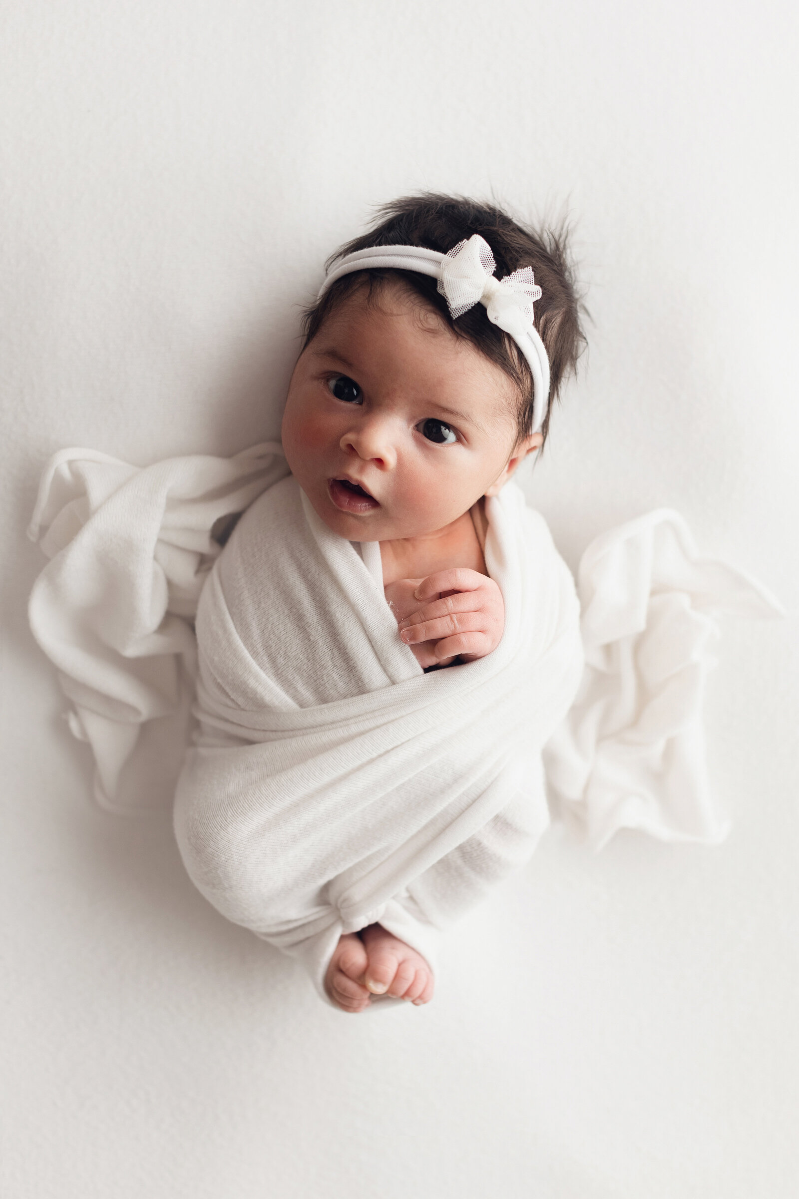 baby girl swaddled in white blanket with white bow in her hair