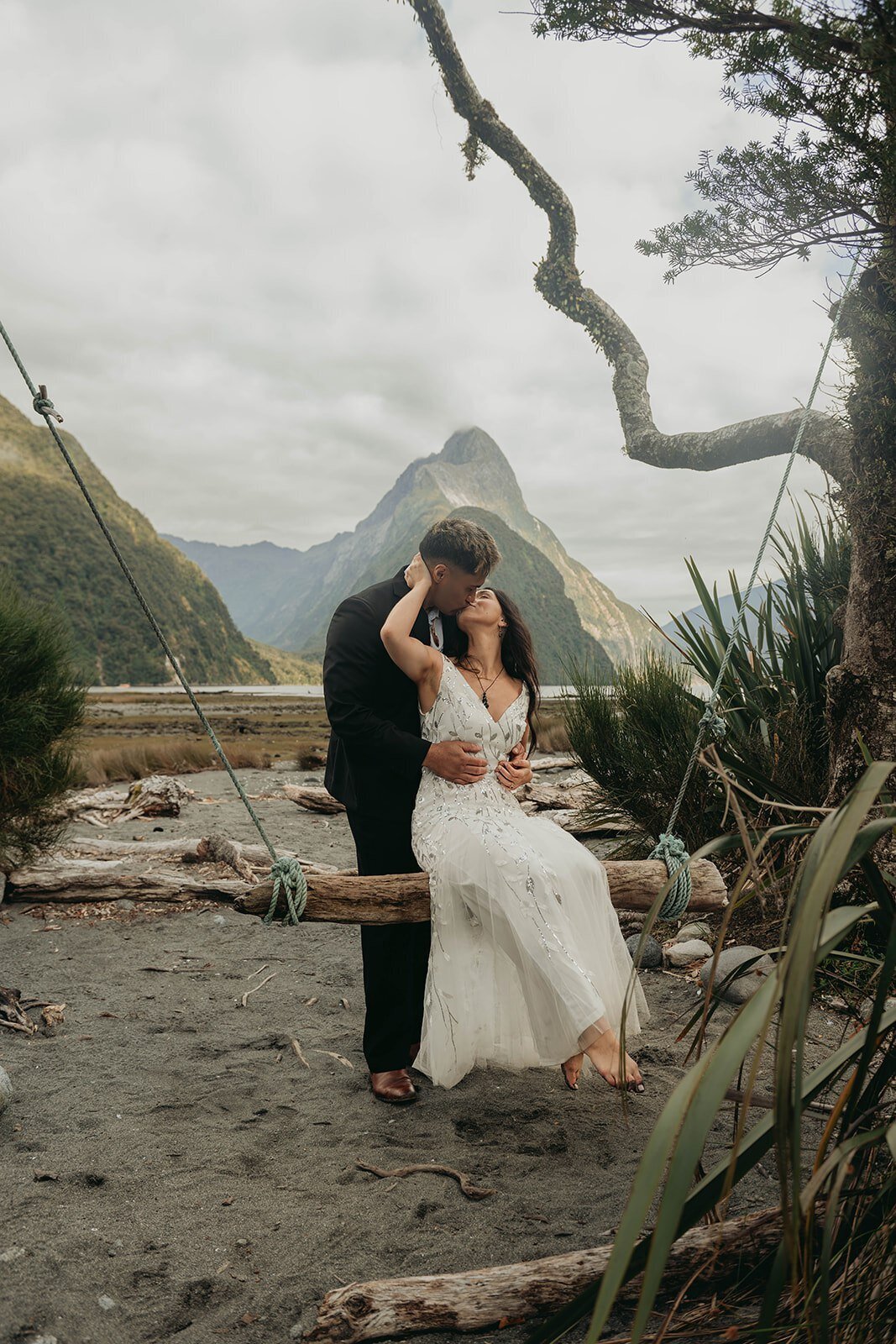 A couple in wedding attire embraces on a swing, with mountains and a cloudy sky in the background—capturing the spirit of a California photography retreat for storytellers and soul seekers.