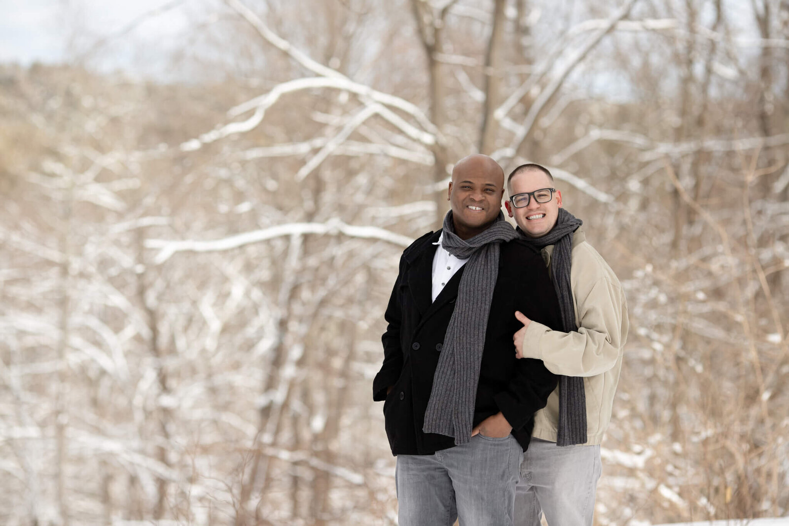 Gay couple posing for photos on the snowy wooded grounds of Long Hill in Beverly MA
