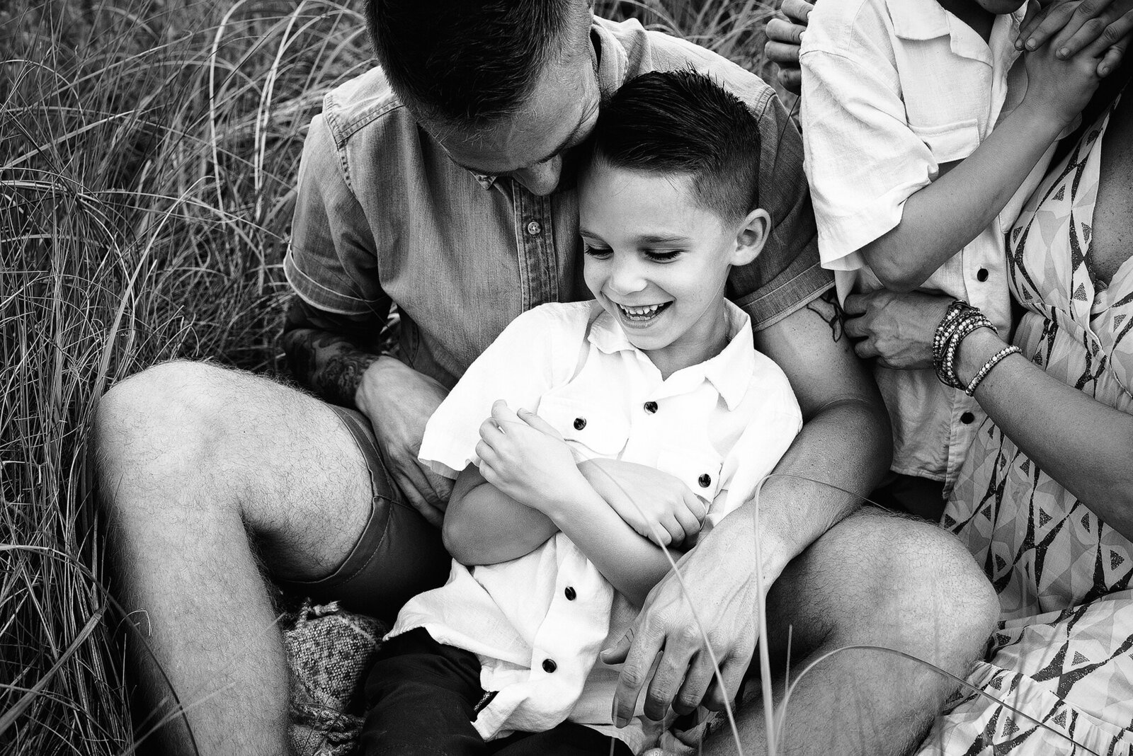 Black and white image of son being tickled by dad in tall grass in Jacksonville, FL.