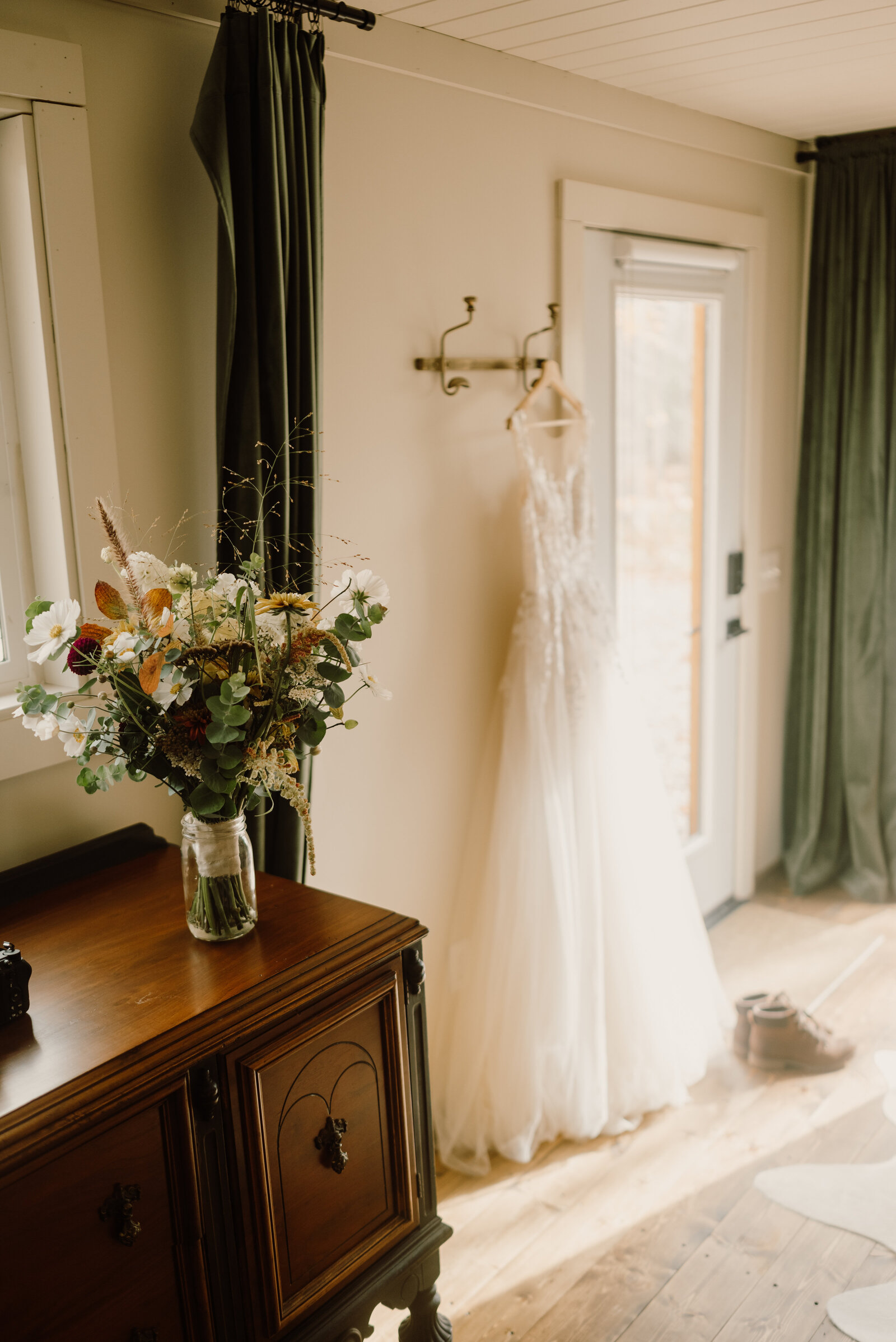 Bridal bouquet placed on vintage dresser with a wedding gown hanging in a cabin