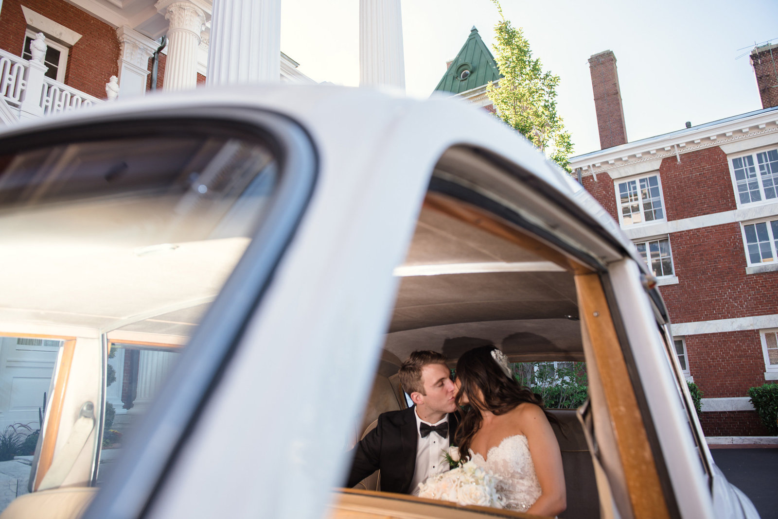 Bride and groom kissing in a vintage car in front of the Bourne Mansion