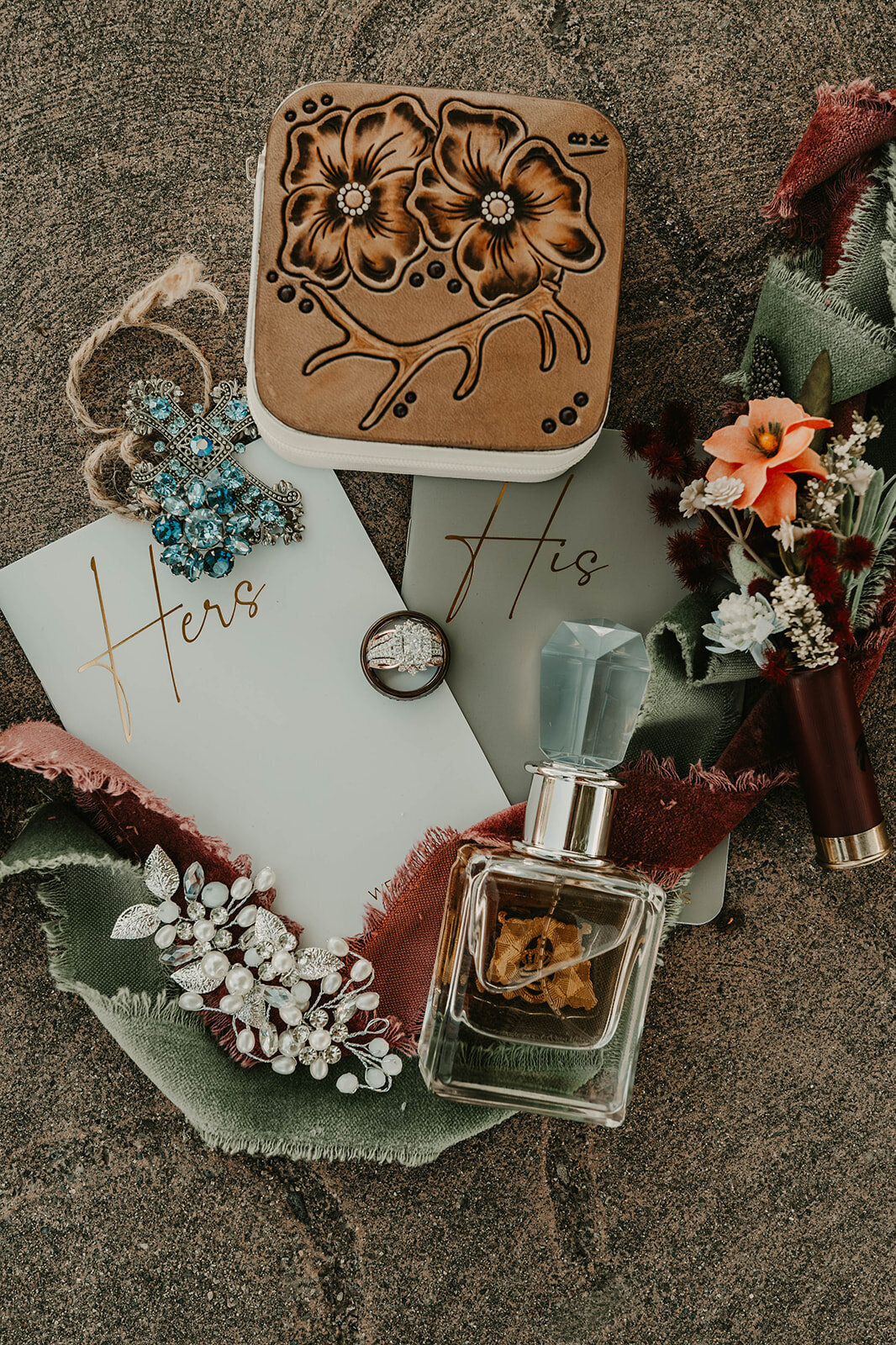 Flat lay of "His" and "Hers" cards, rings, perfume, flowers, jewelry, and a floral-embossed box on fabric—perfect details for a Colorado wildflower elopement beautifully captured by a Colorado elopement photographer capturing real connection.