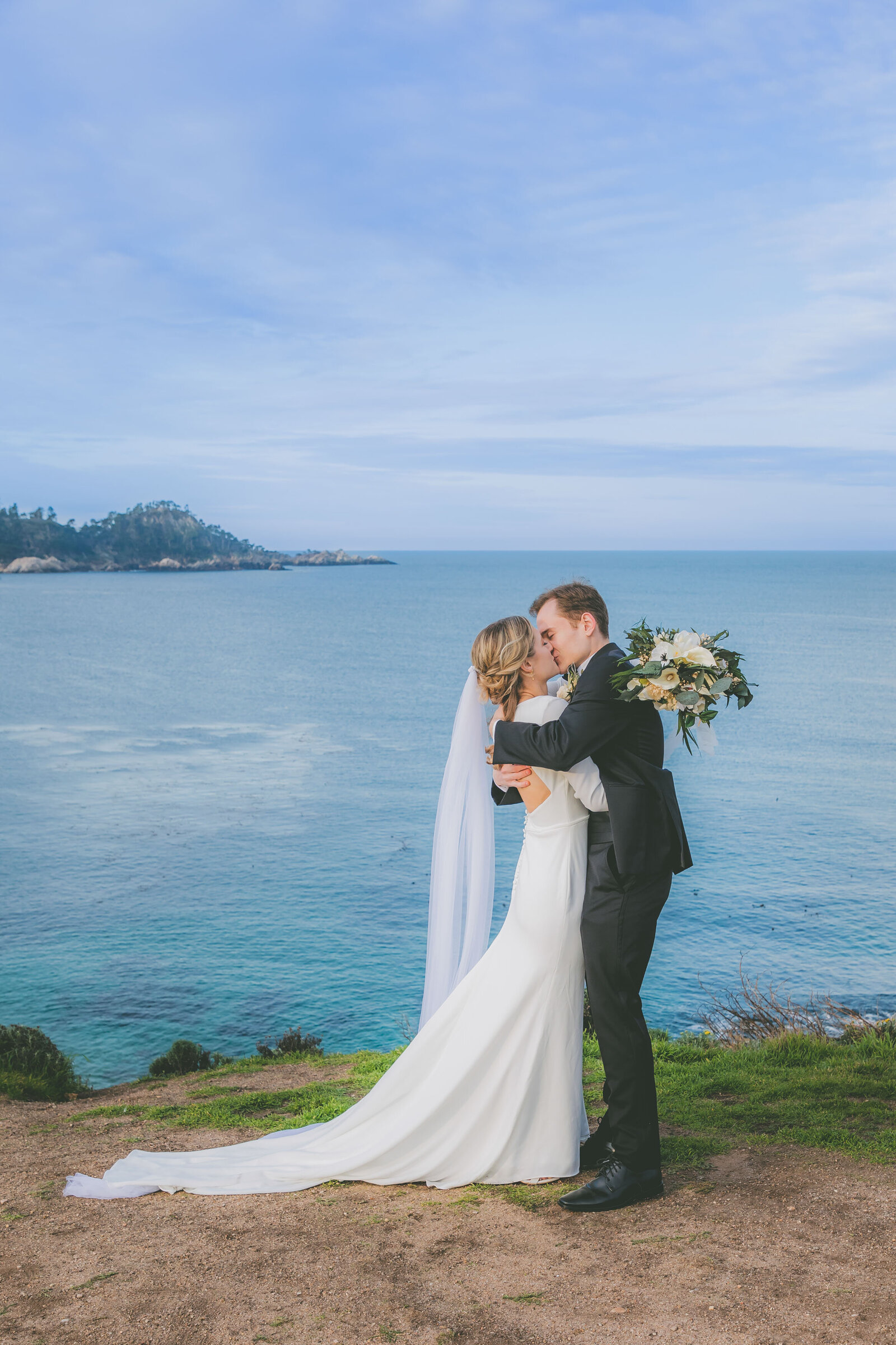 Newlyweds kiss with an ocean view in the background during their sunrise elopement..