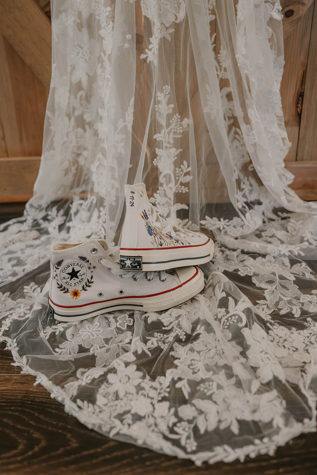 White Converse shoes with floral embroidery rest on white lace fabric with a floral pattern, perfect for a Colorado wildflower elopement.