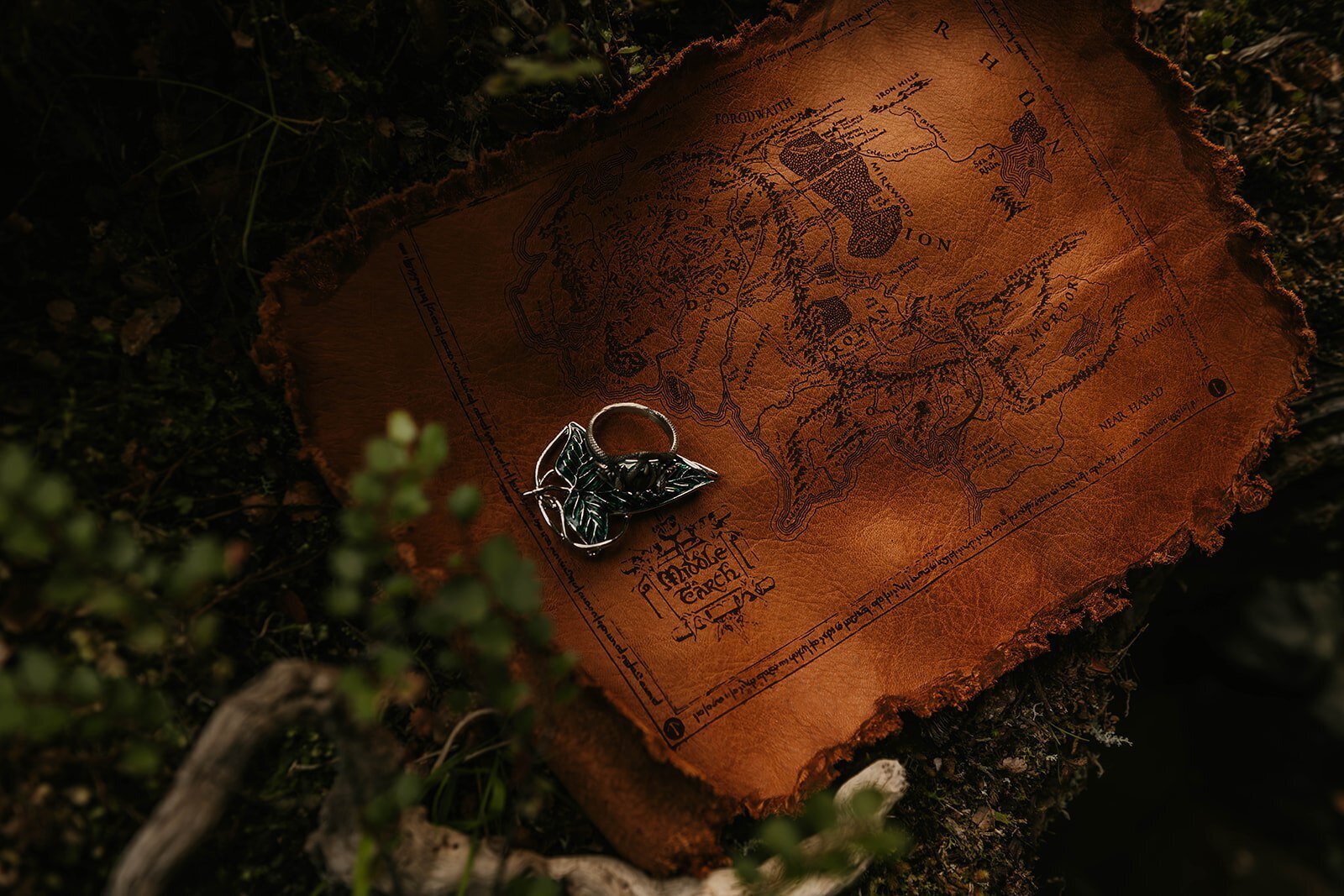 A silver leaf brooch rests on a worn, fantasy-style map placed on mossy ground—an image evoking the spirit of a Switzerland photo retreat in the Alps for adventurous photographers.