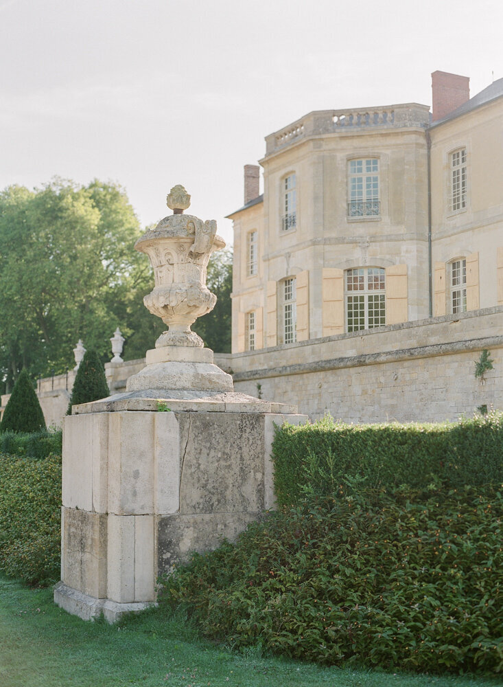 Large stone cream statue with off white chateau behind it
