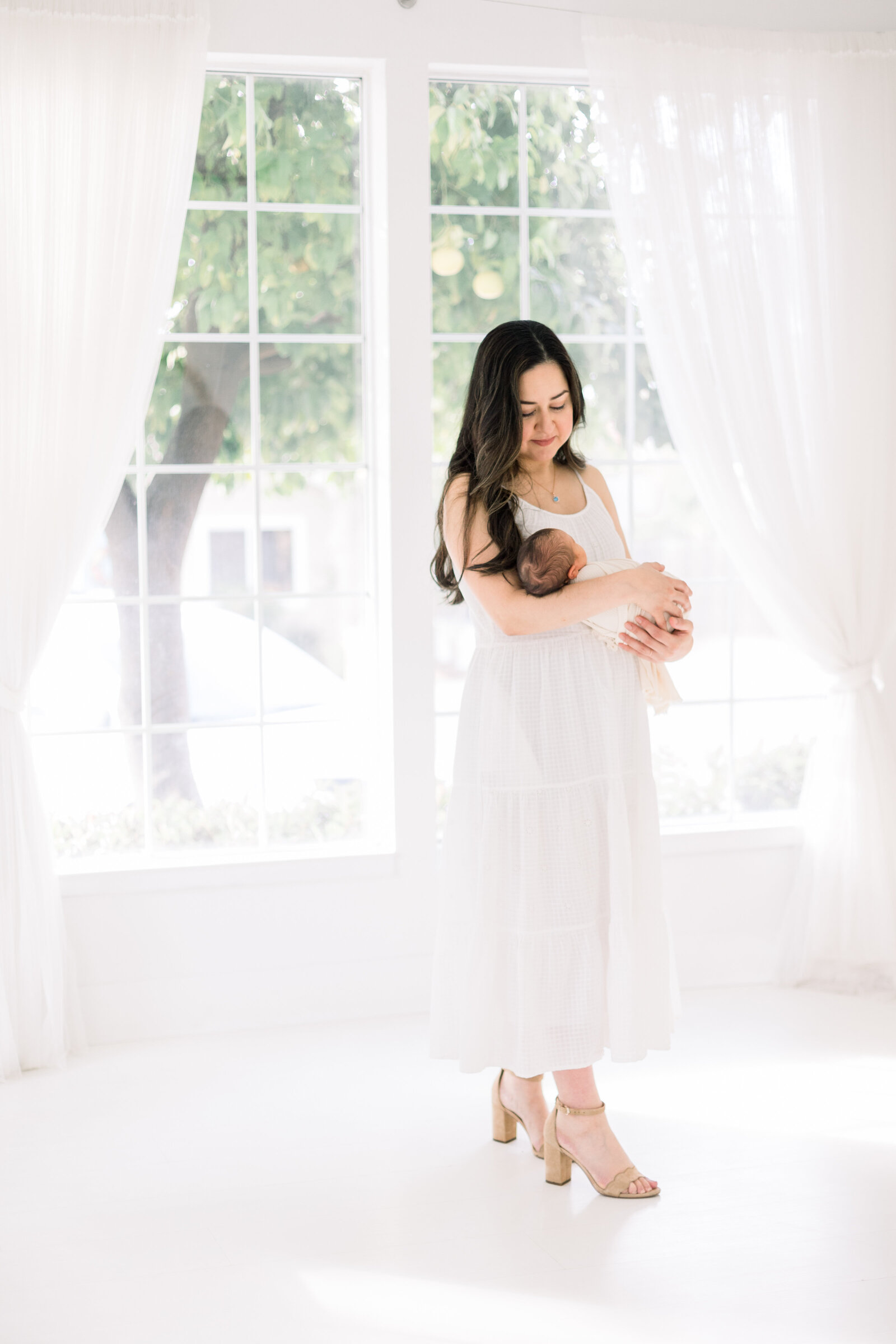 Image of new mother standing by window holding her newborn baby taken by Newborn Photographer Sacramento Kelsey Krall