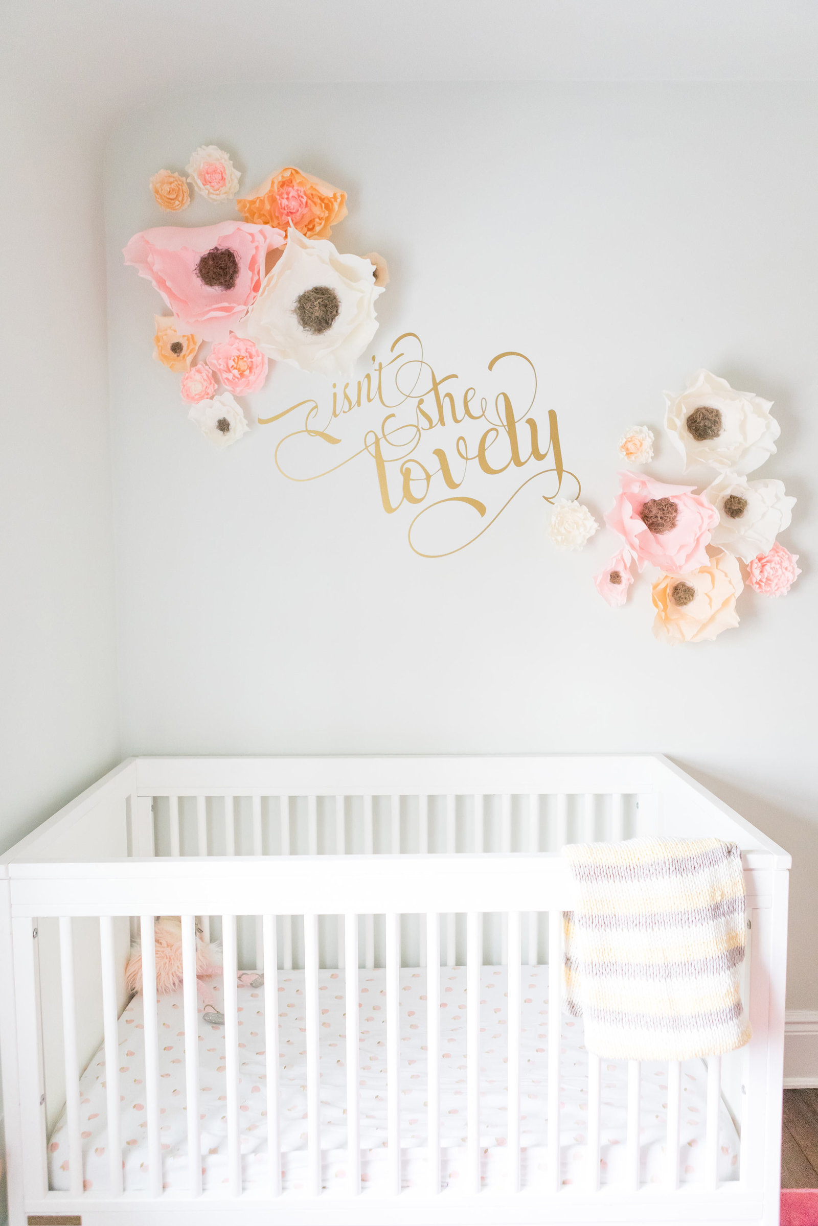 A crib with 3D paper flowers and gold quote.