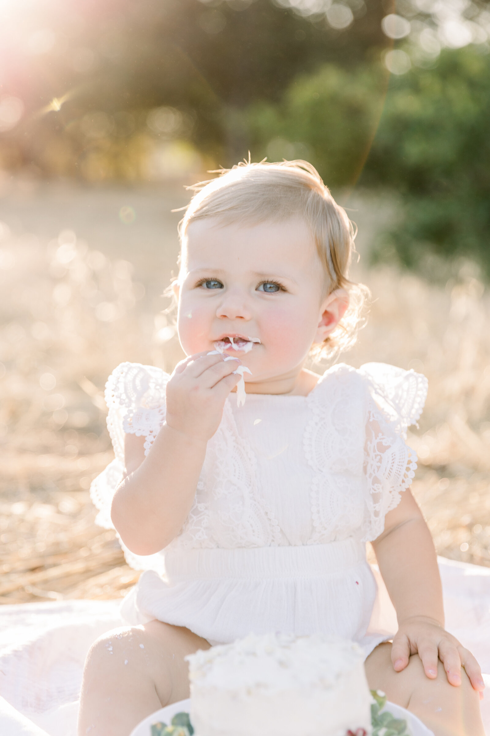 Image of one year old baby girl wearing white eating her cake taken by Sacramento Newborn Photographer Kelsey Krall