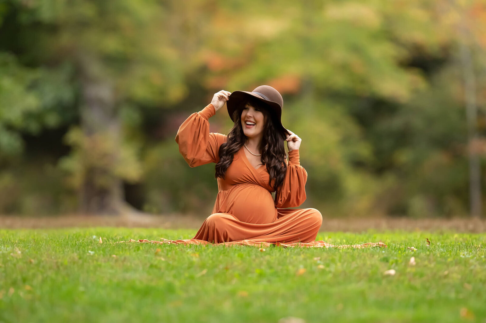 Pregnant mother sitting in grass holding on to her oversized hat