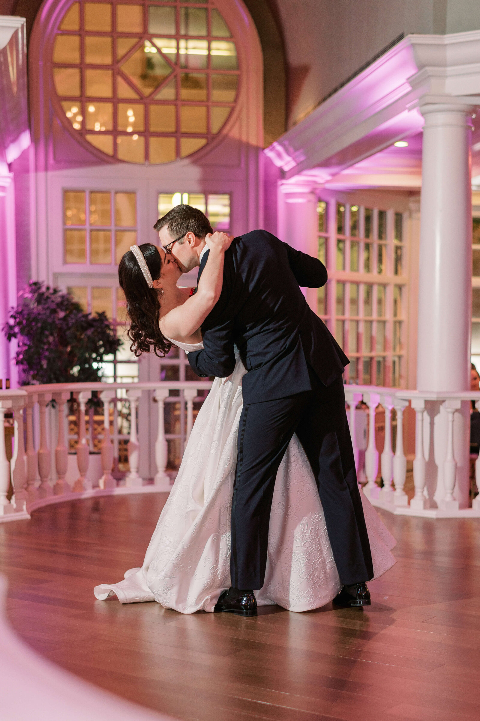 Purple up lighting frames the bride and groom during their first dance while the groom dips and kisses the bride