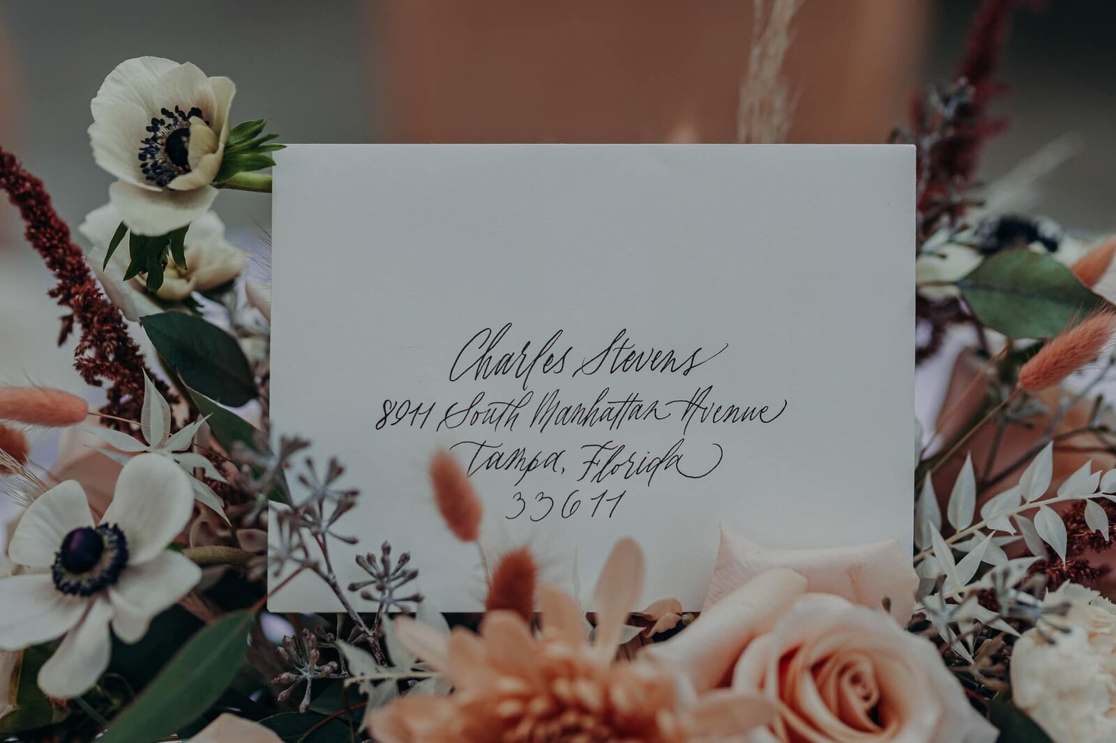 white modern calligraphy envelope tucked in a bouquet of wildflowers