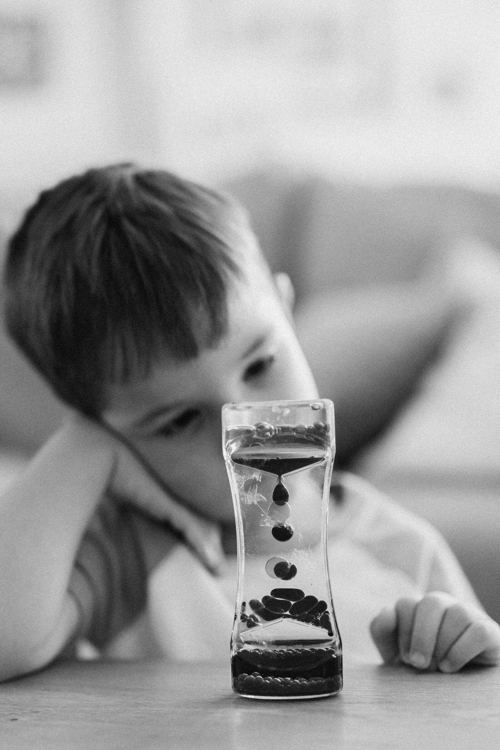 A little boy stares at an hourglass with his head resting in his hands