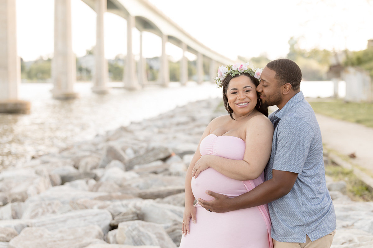 pregnant couple embraces underneath Annapolis bridge
