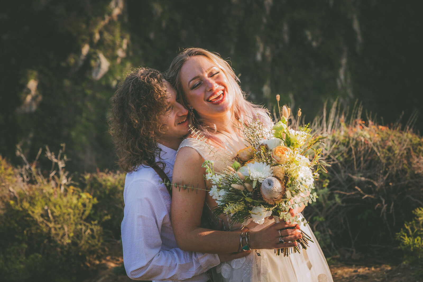 A groom whispers something funny to a bride during their Bixby Bridge portrait session.