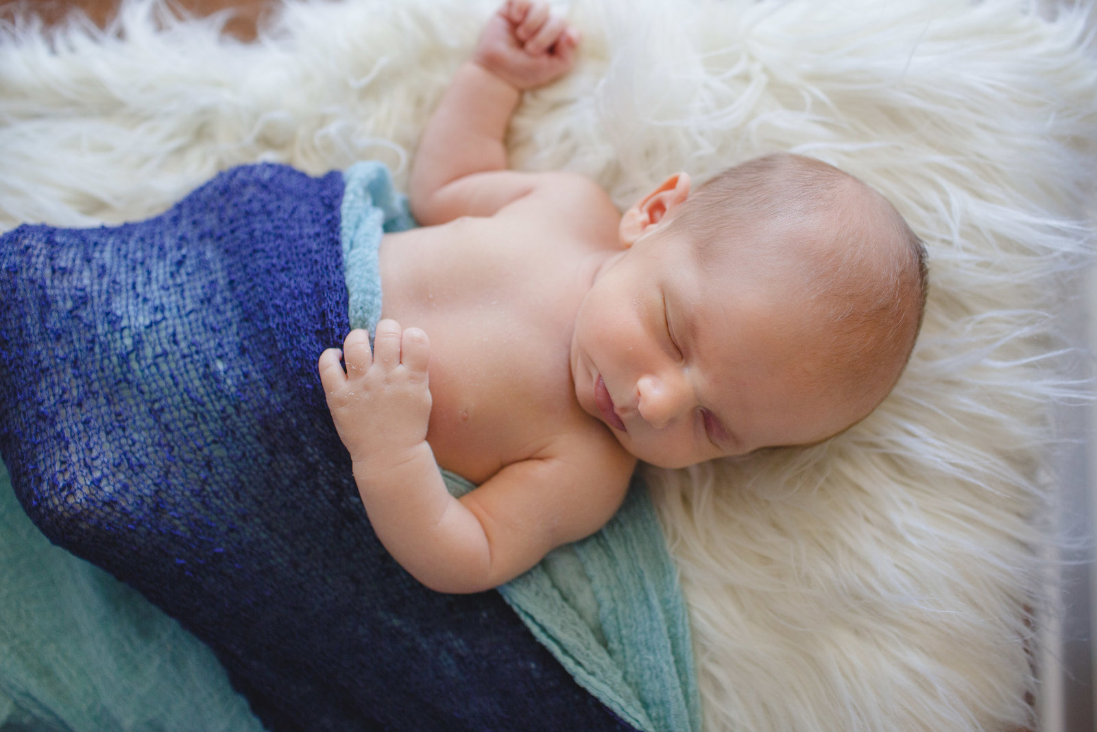 newborn baby boy sleeps on white fur rug