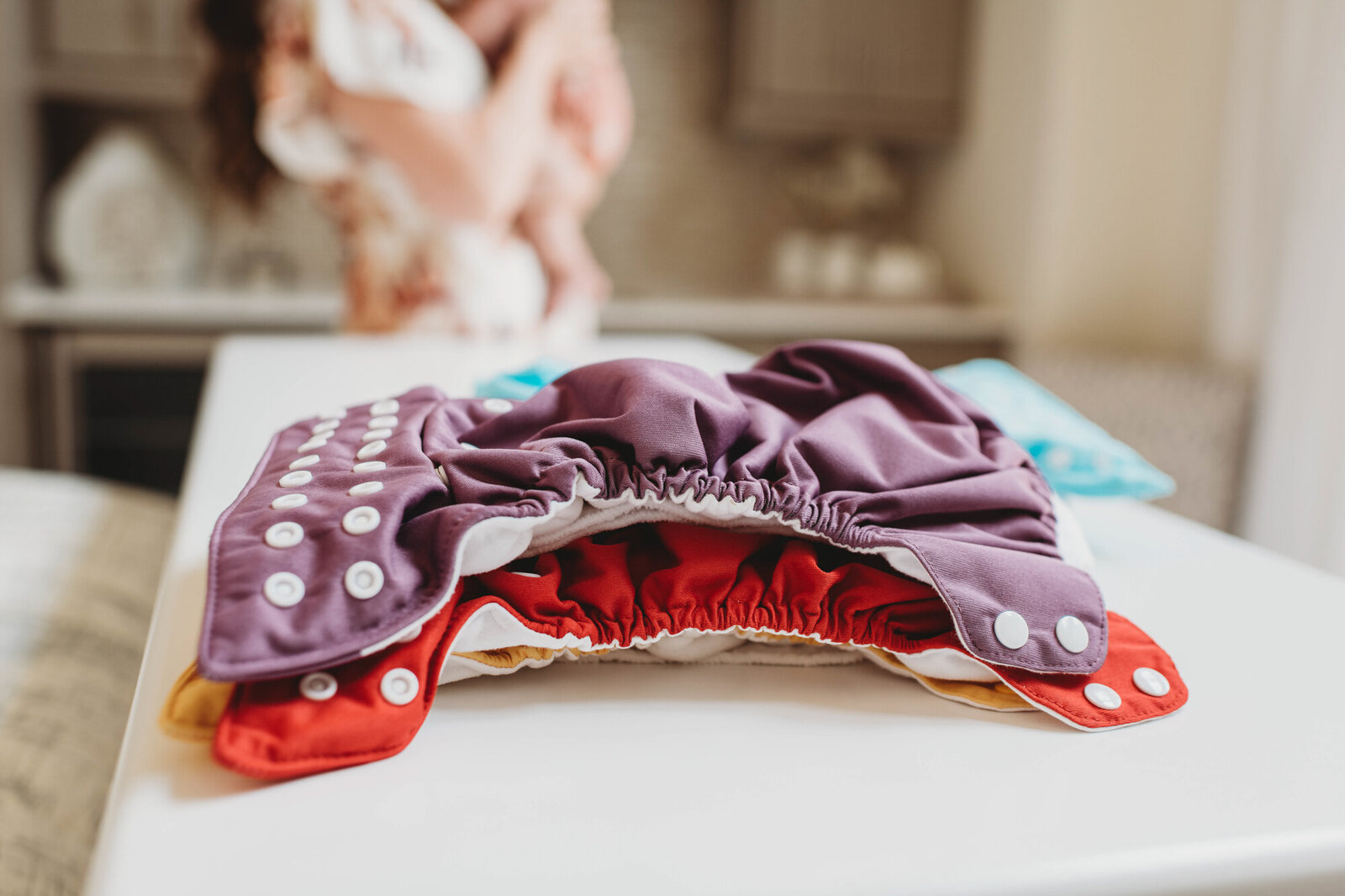 Branding Photographer,  baby clothes are laid on a table in a nursery, mother is with child in the distance