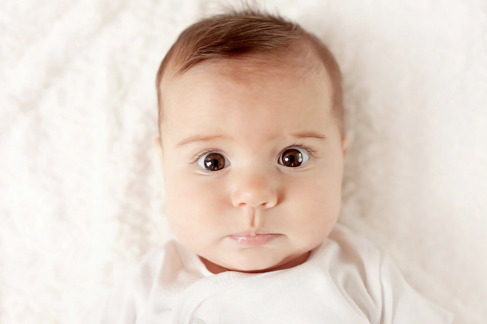 Adorable close-up of a baby with huge brown eyes looking directly into the camera.