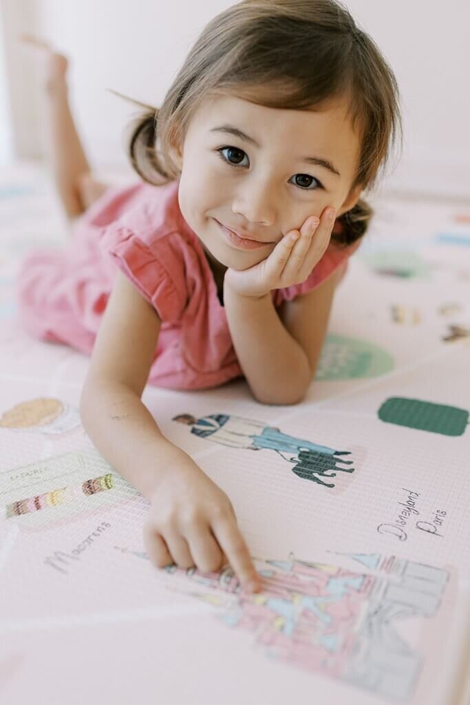 Girl laying down for a play mat brand photoshoot, pointing at a drawing.