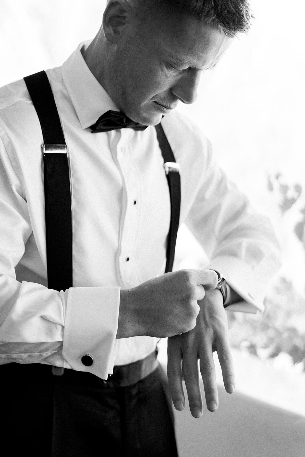 Black and white film photo of groom adjusting his watch during wedding prep at Hummingbird Nest Ranch.