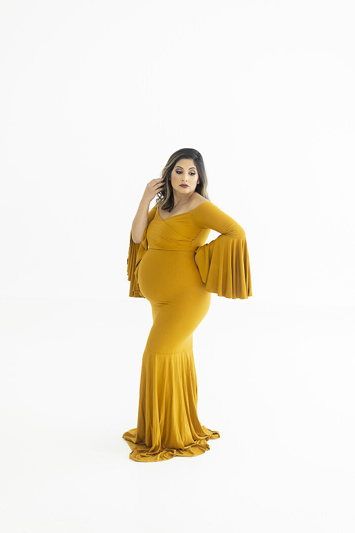 Pregnant mother wearing yellow maternity gown in white studio.