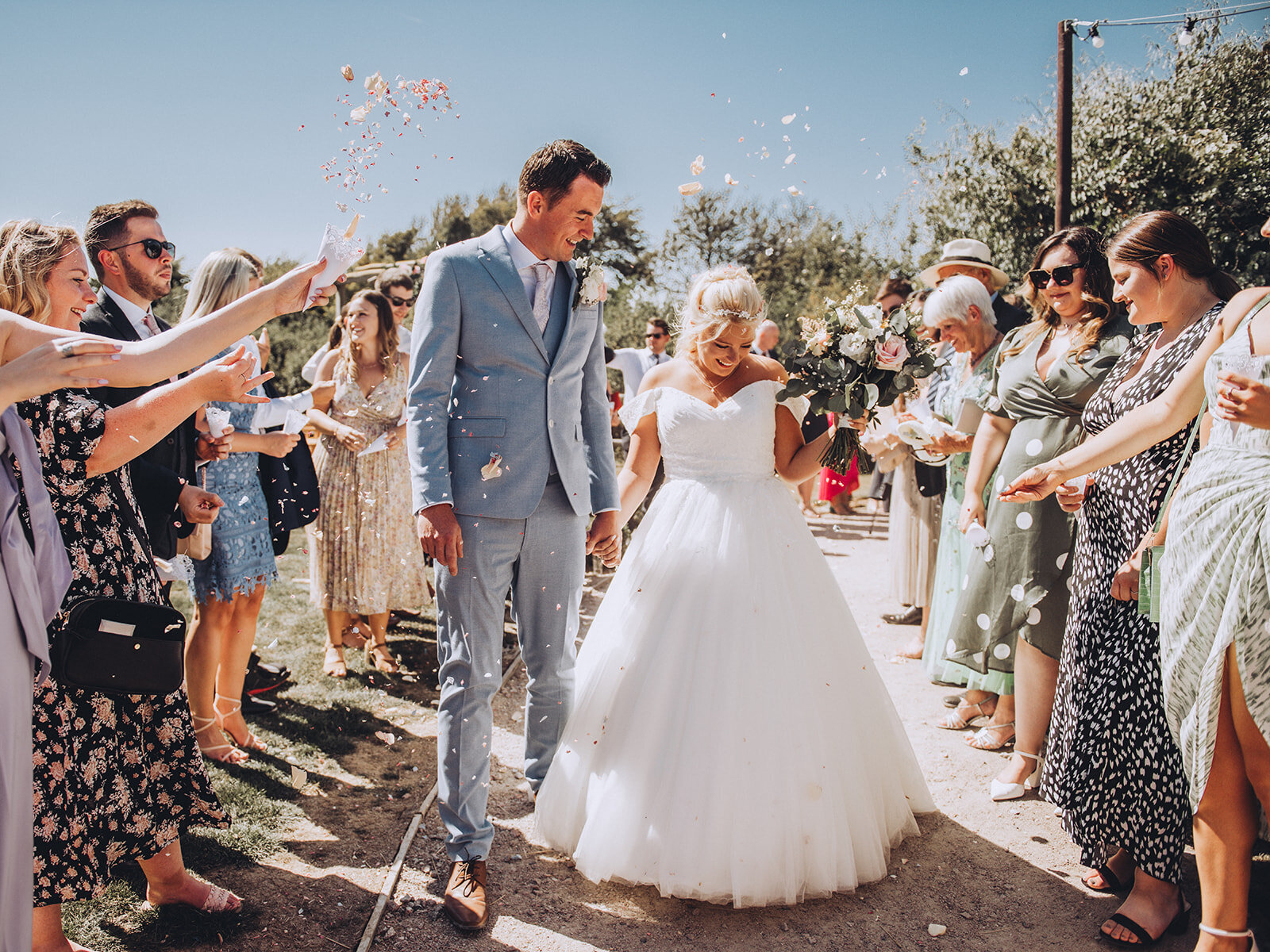 Newlywed couple walk through pastel coloured confetti at their wedding at Reach Court Farm