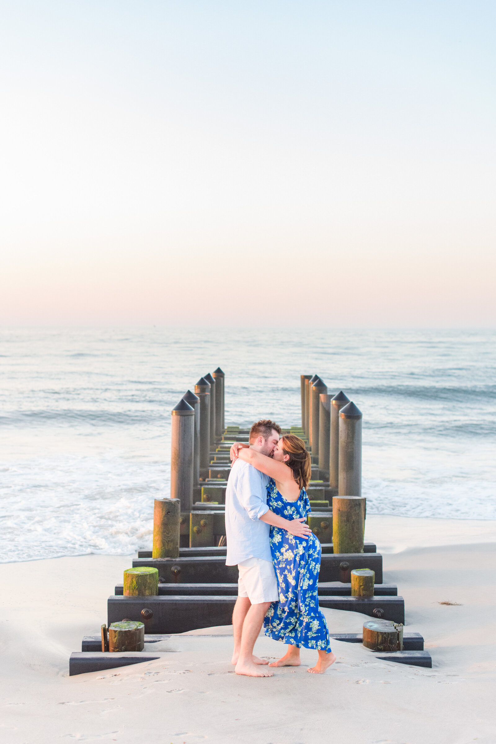 Couple kisses and embraces on the shore line of Cape May at sunrise during their Cape May engagement session