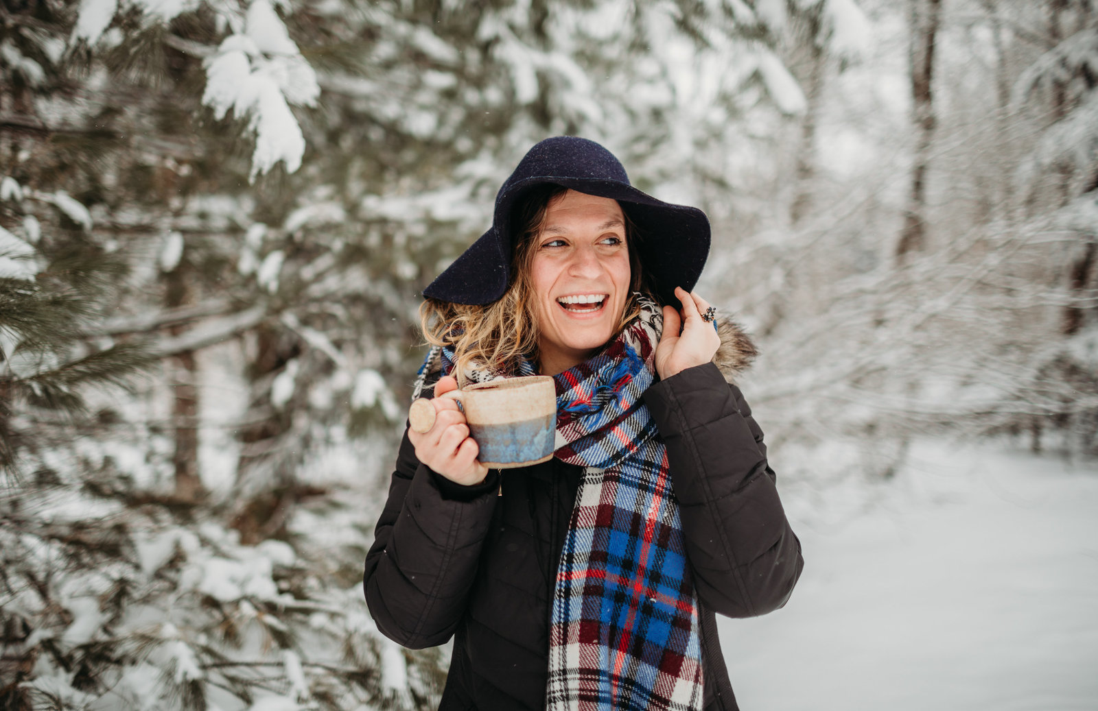 woman stands in snow with coffee mug and laughs during personal brand photos