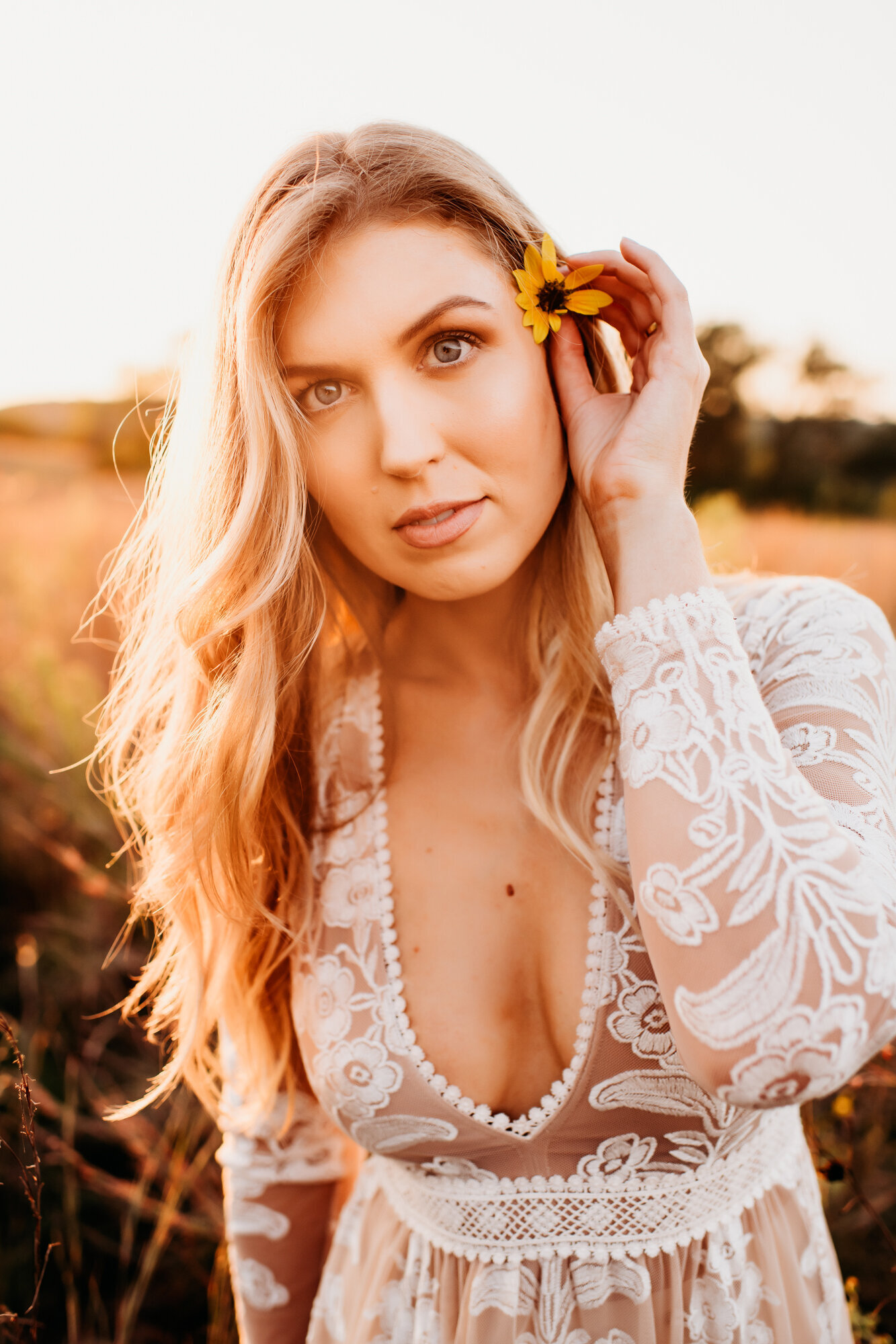 Branding Photographer, a woman in a lacy dress places a daisy in her hair at golden hour outside