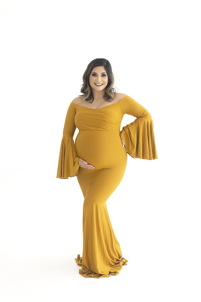 Pregnant mother wearing yellow maternity gown in white studio.