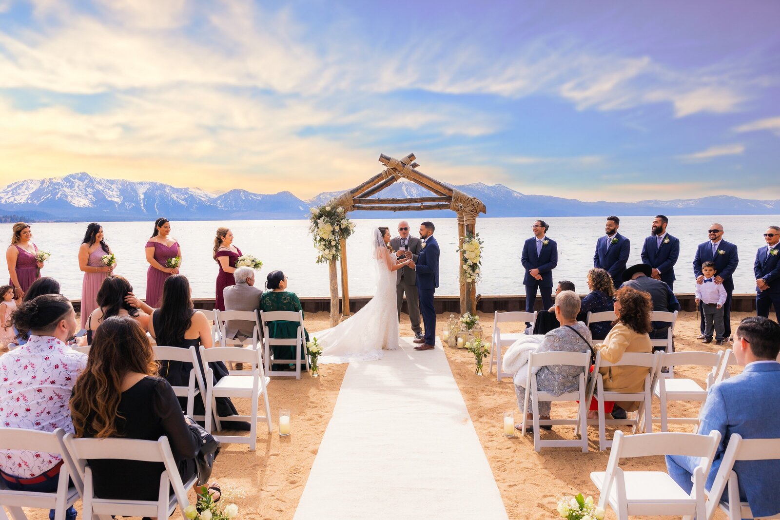 Bride and groom exchange vows in front of Lake Tahoe on the beach with guests looking on. Wedding photography studio, philippe studio pro captured the moment.