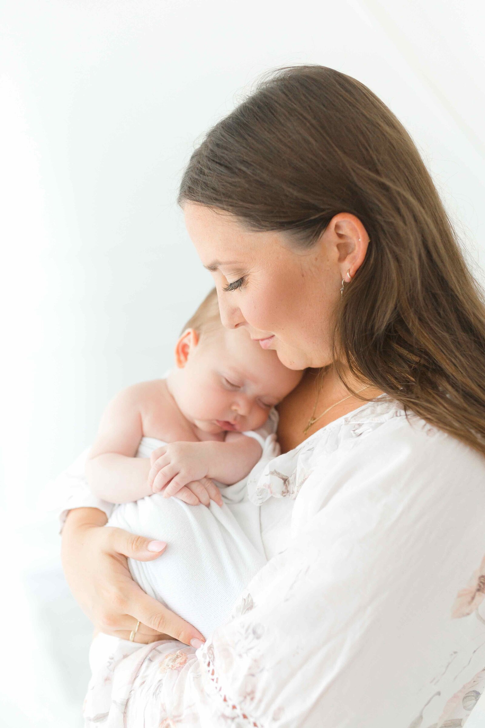 Neugeborenenfotoshooting: Mama in weißem Kleid hält ihr schlafendes Baby im Arm.