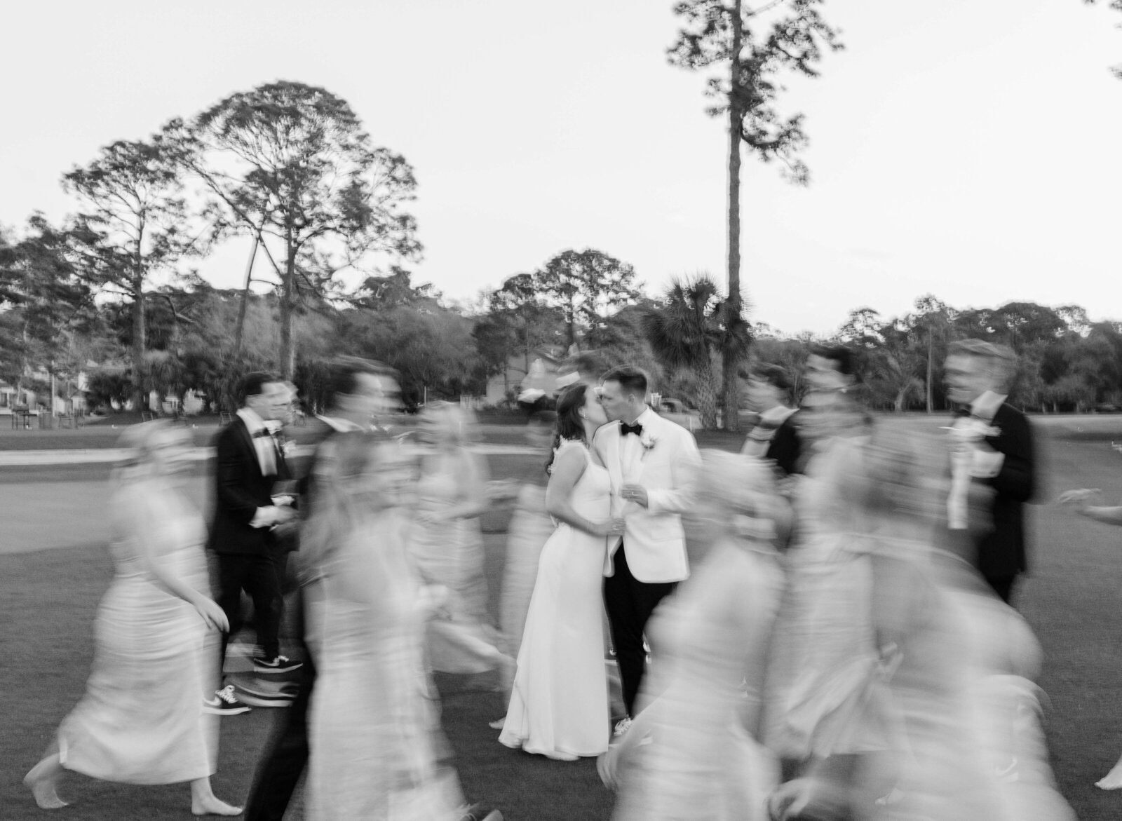 A couple kisses while their bridal party walks past in a blur