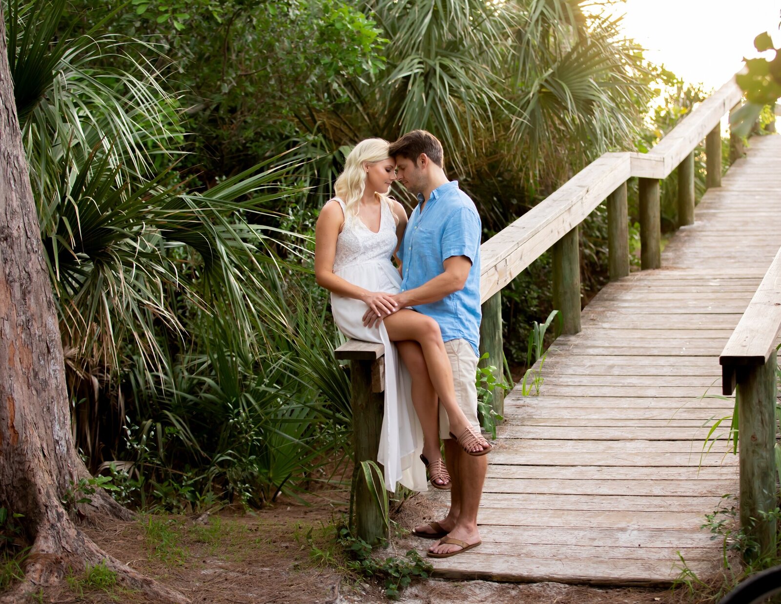 Recently engaged couple sitting on the railing heading out to Bean Point Beach on Anna Maria Island