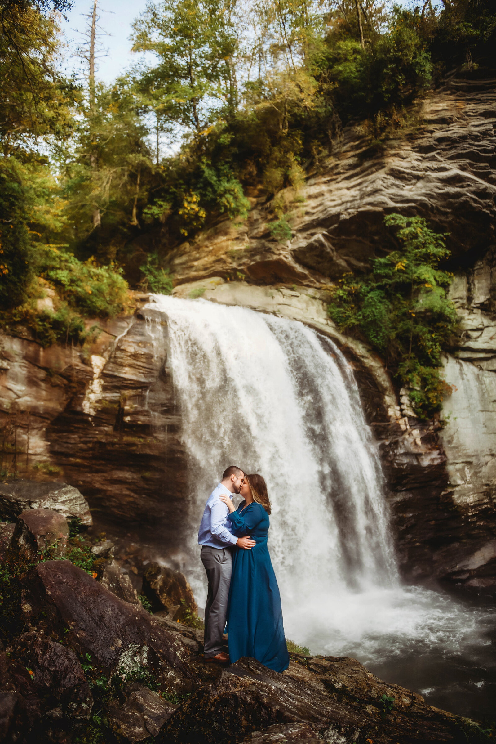 Couple kisses in front of Looking Glass Falls while posing for Engagement Photos near Asheville, NC.