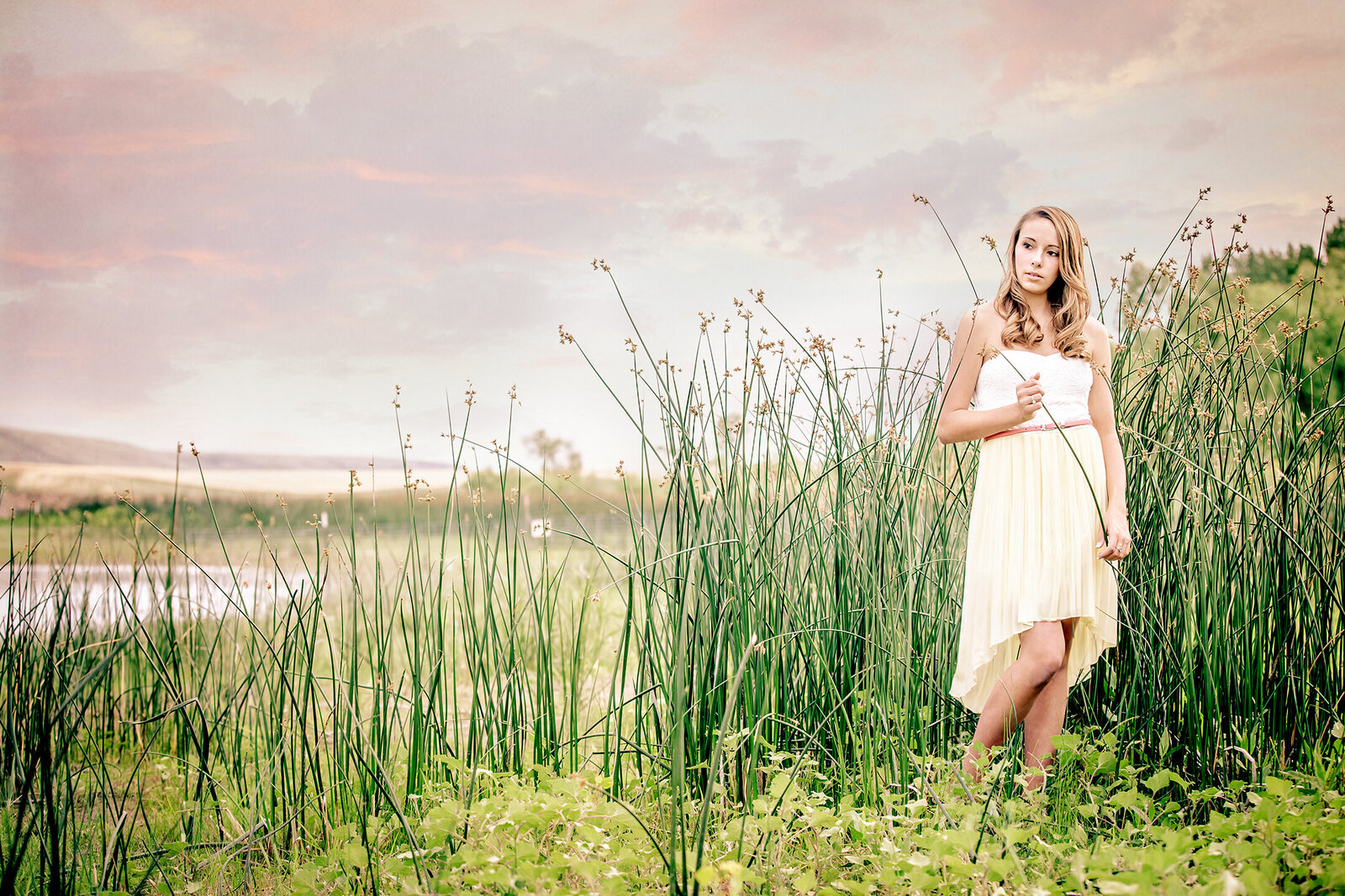 High school senior pictures. Picture of a girl in a white dress standing in the green cattails next to the river. Photographers in Billings, MT.