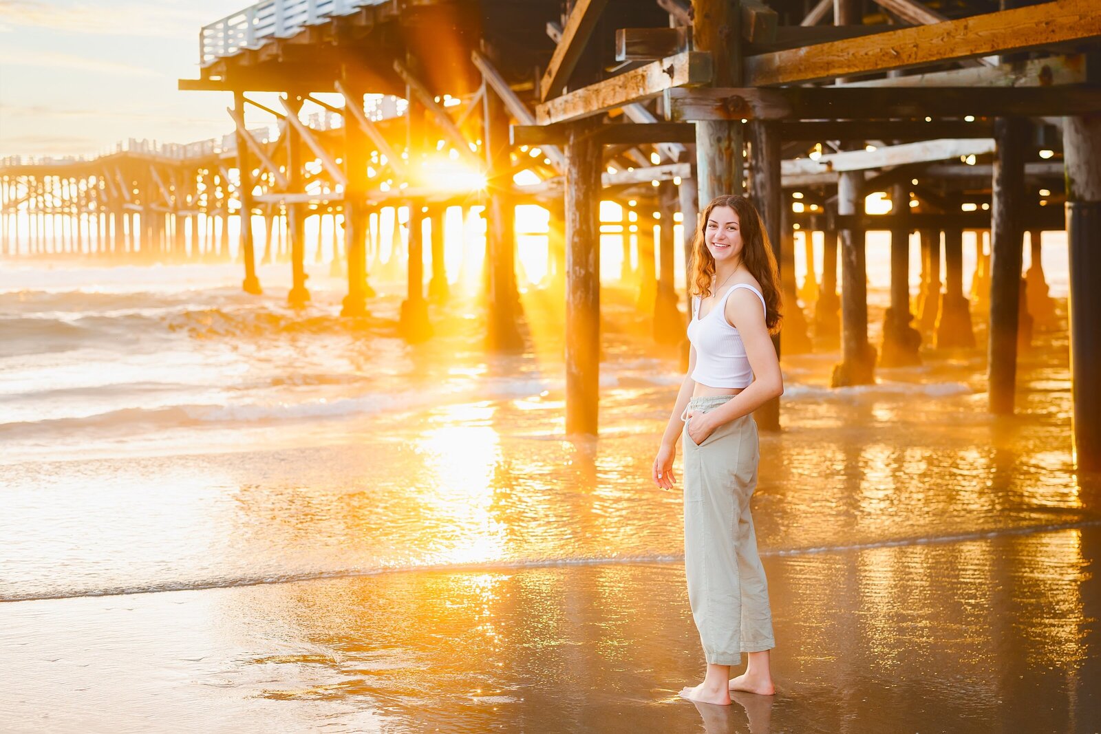 Senior girl posing by Crystal Pier with the sun bursting through the pier