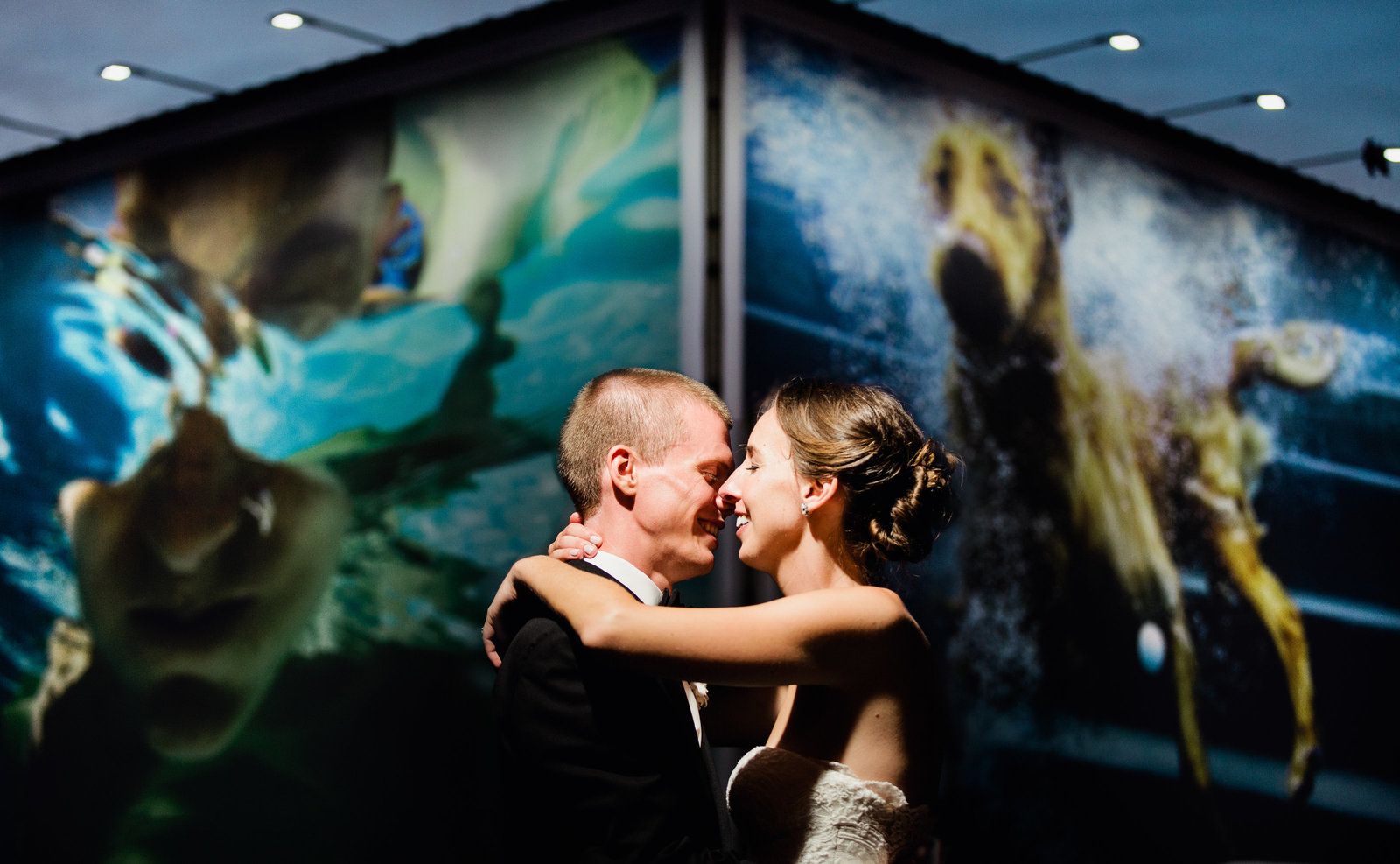 a downtown Columbus wedding photo taken at night of a couple in front of a colorful billboard with a dog and swimmer underwater