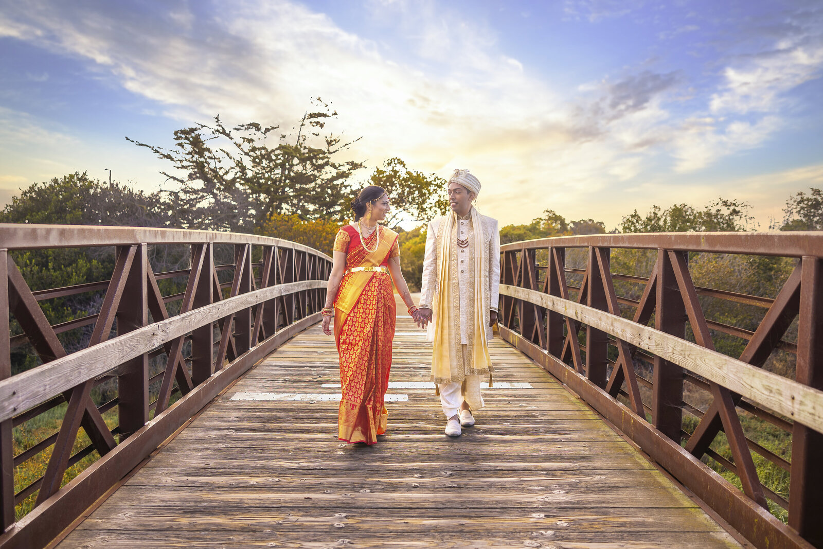 bride and groom walk across a bridge holding hands and smiling each other with beautiful sunrise in the distance. Captured by Sacramento photography studio, Philippe Studio Pro.
