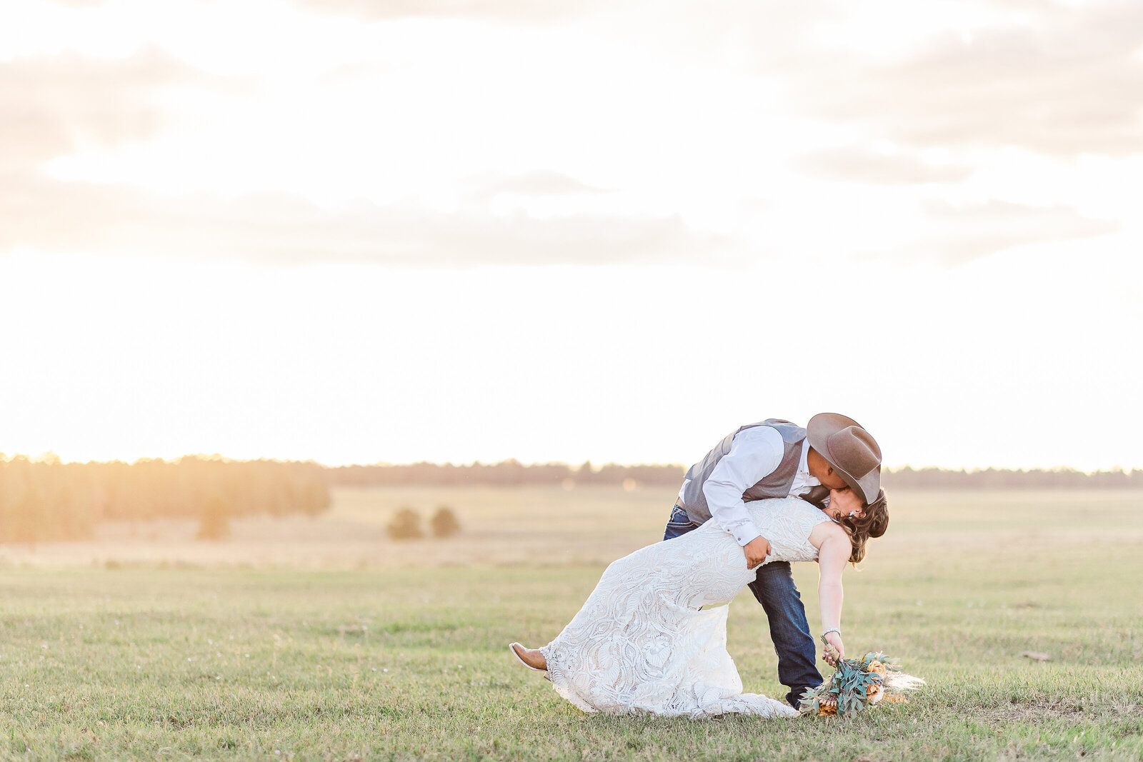 Groom dipping bride in field