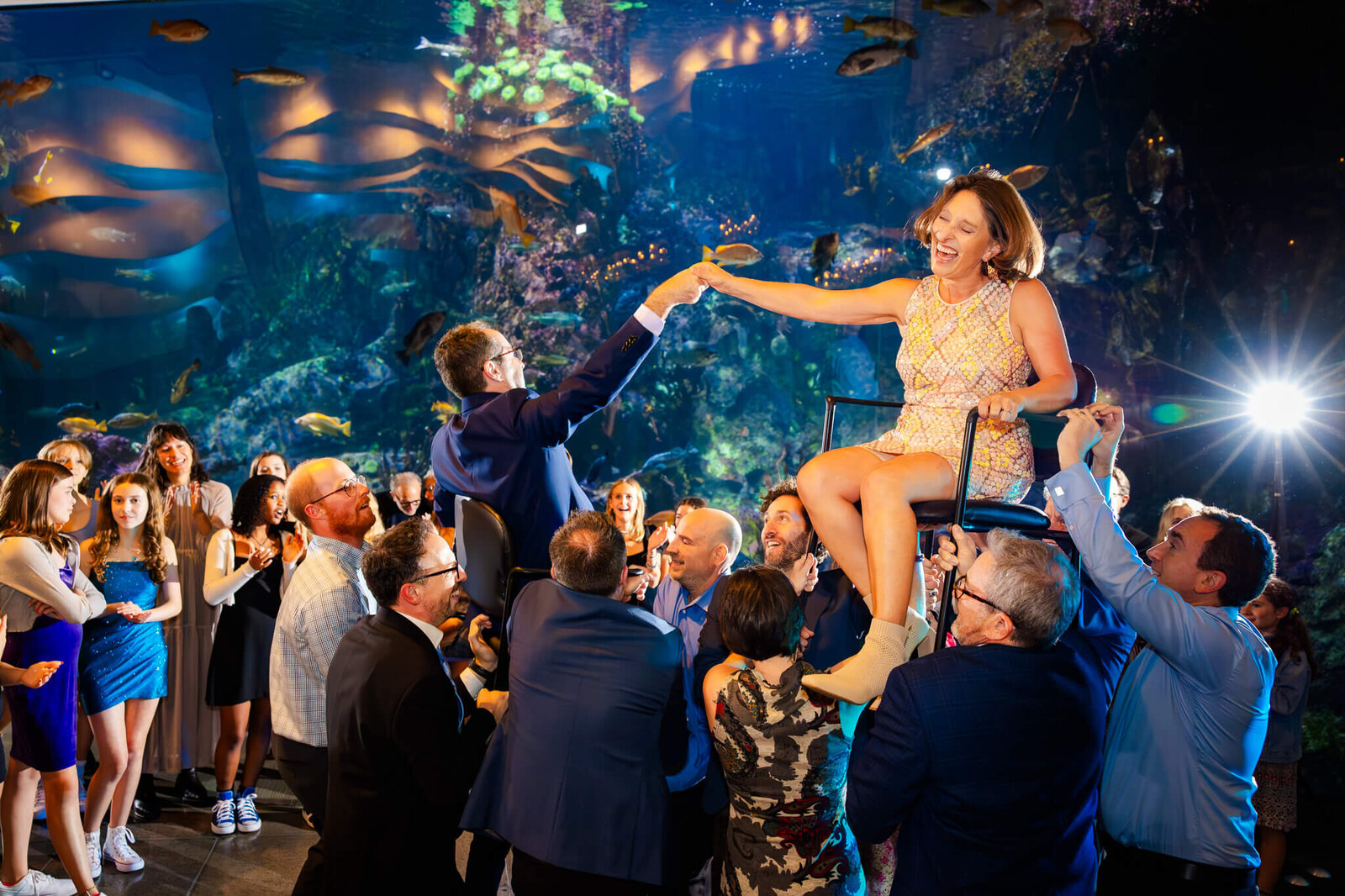 A happy woman lifted in a chair celebrates on the dance floor with her teen son in an aquarium.