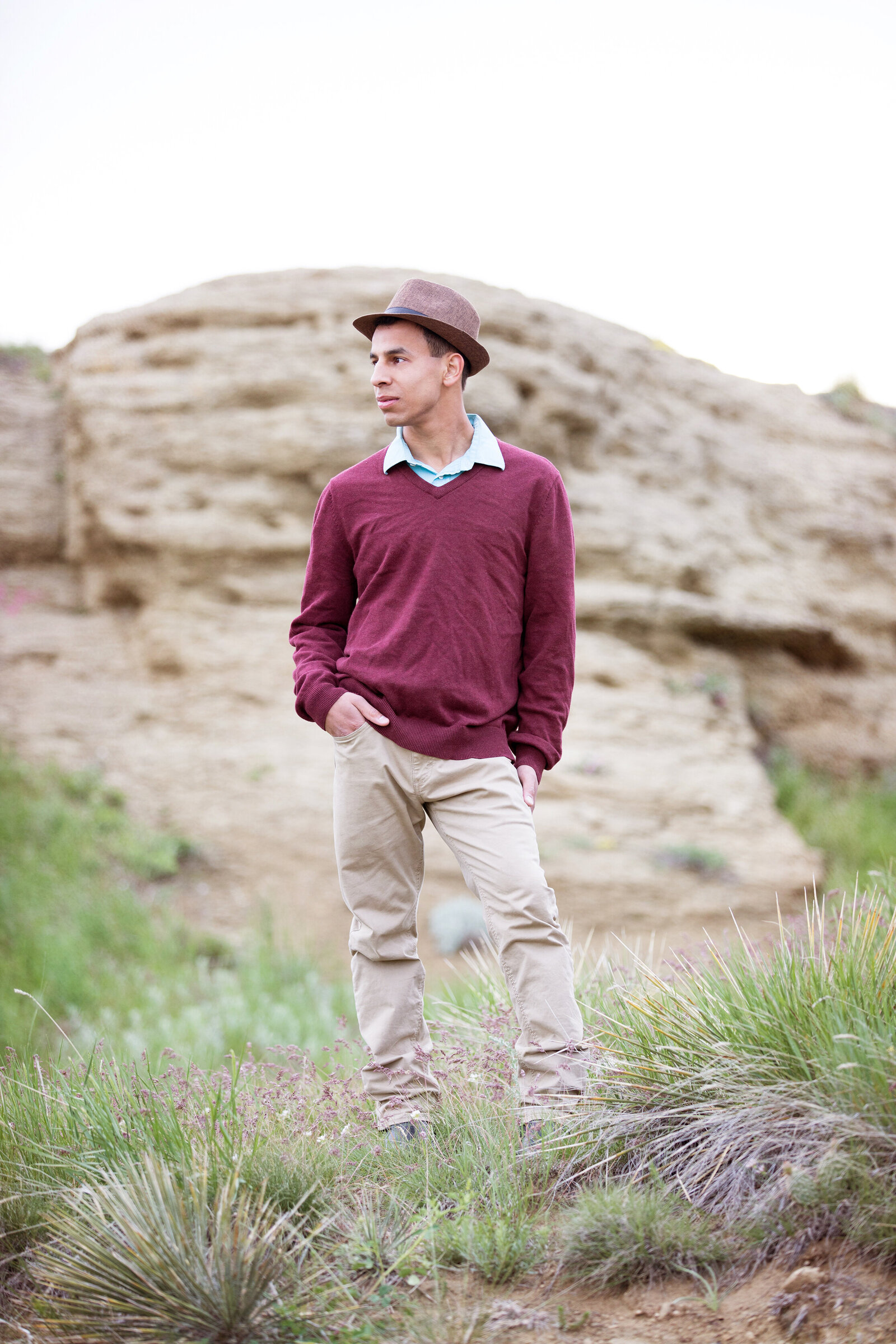 Picture of  high school senior wearing red and tan and a hat. Yucca plants in the foreground and sandstone in the background at Swords Park near the airport in Billings MT.